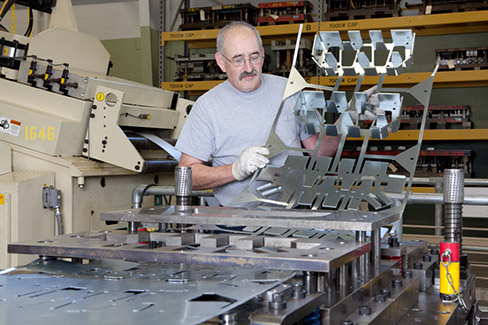 A Larson Tool & Stamping employee inspecting a strip from a progressive die.