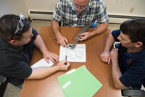 Three Larson Tool & Stamping employees sitting around a table reviewing design specifications for a custom tool.